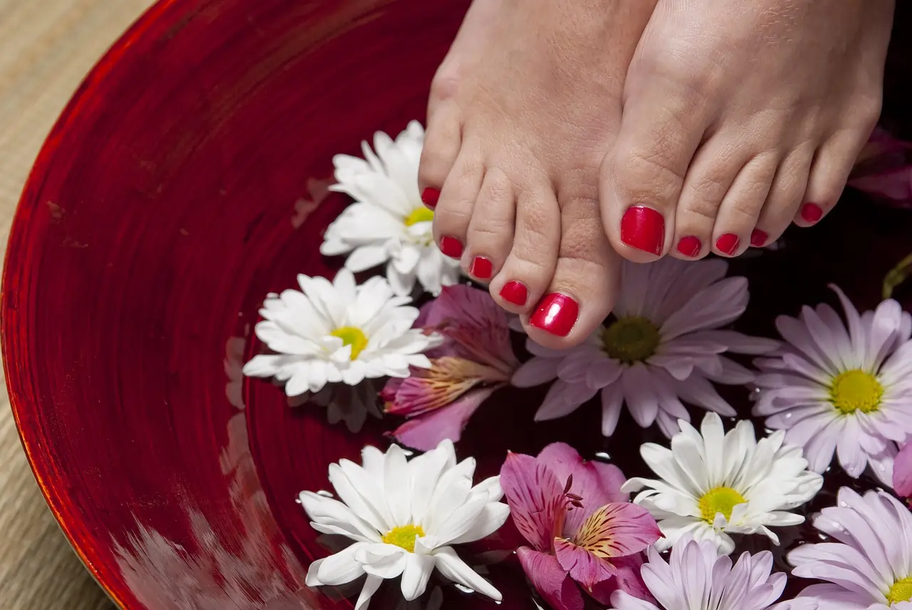A pair of pedicured feet above a basin of water with floating lotus blossoms.