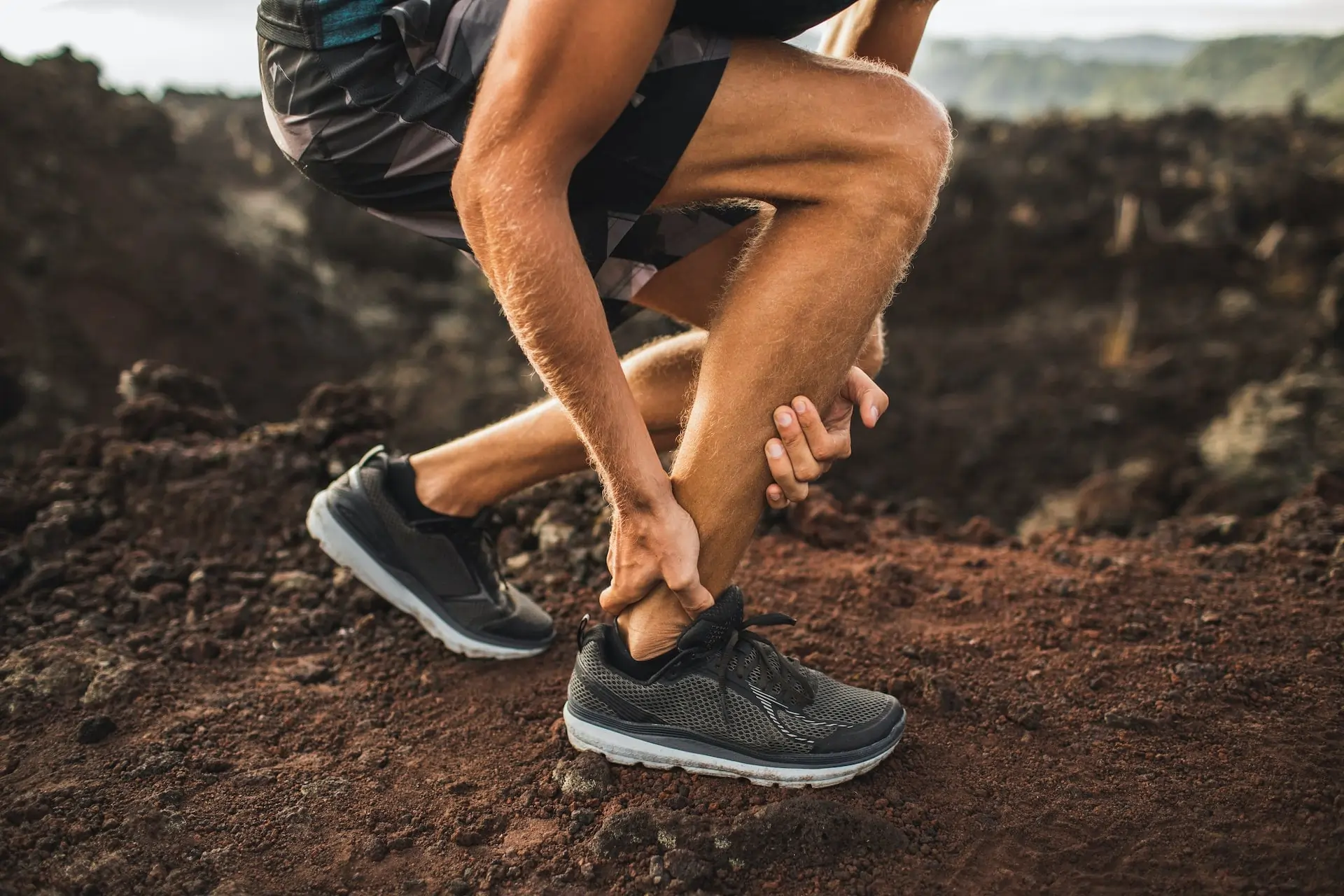 A man, half-kneeling while clutching his right ankle with both hands.