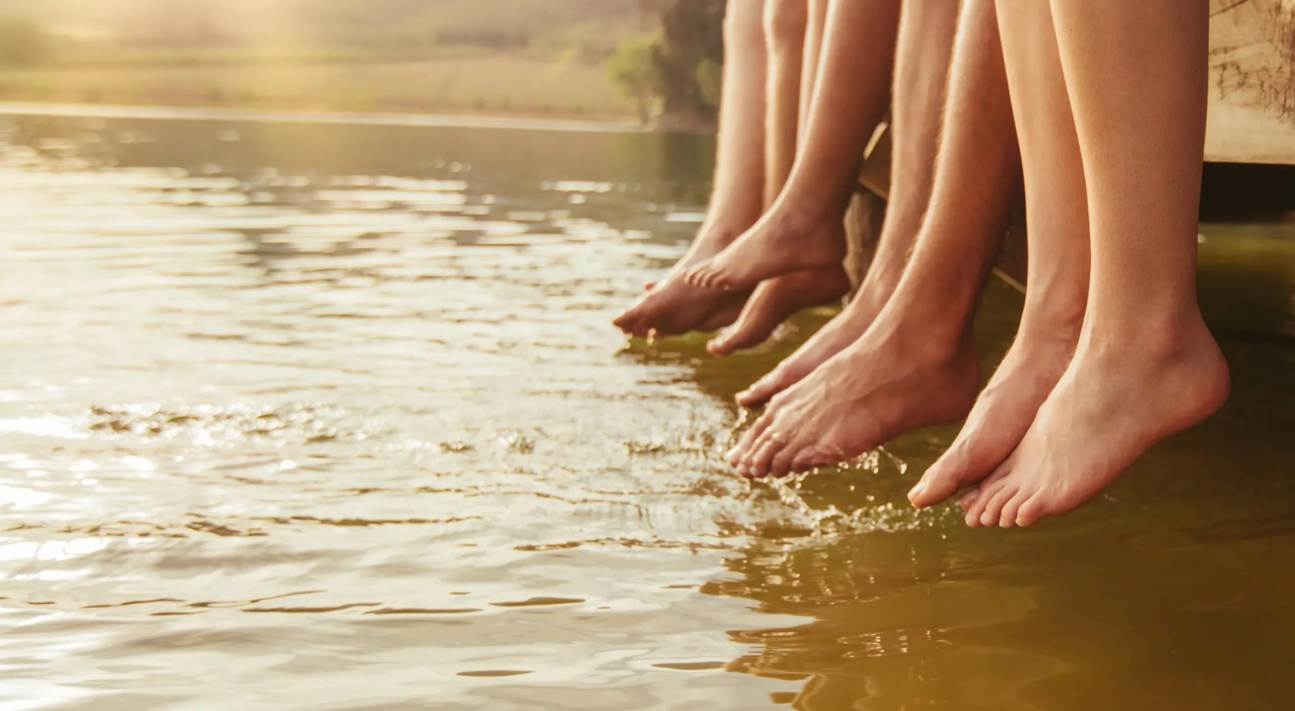 Several pairs of feet dangling over a body of water during twilight.